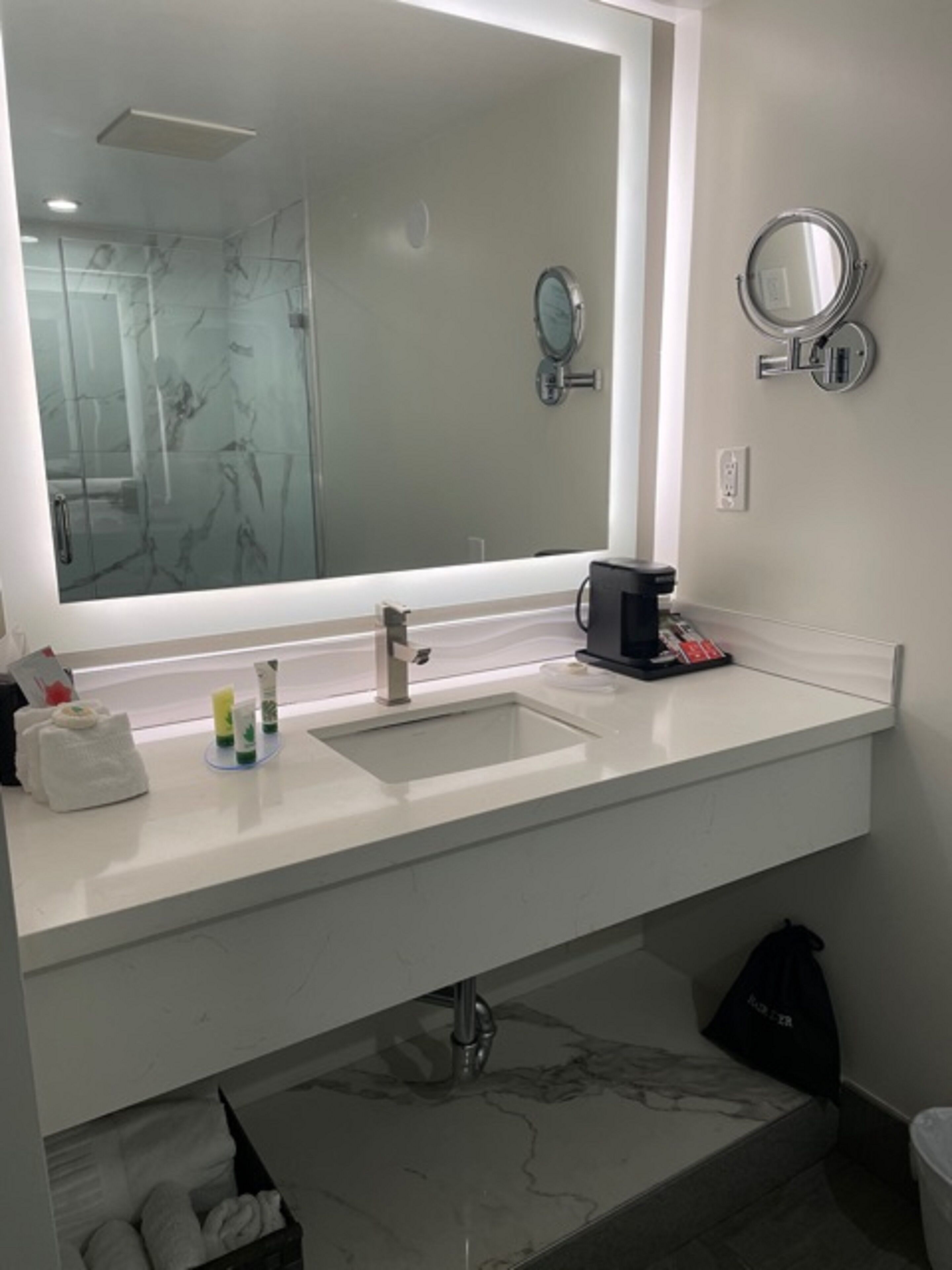A modern bathroom with a large mirror, two sinks, and a coffee machine.