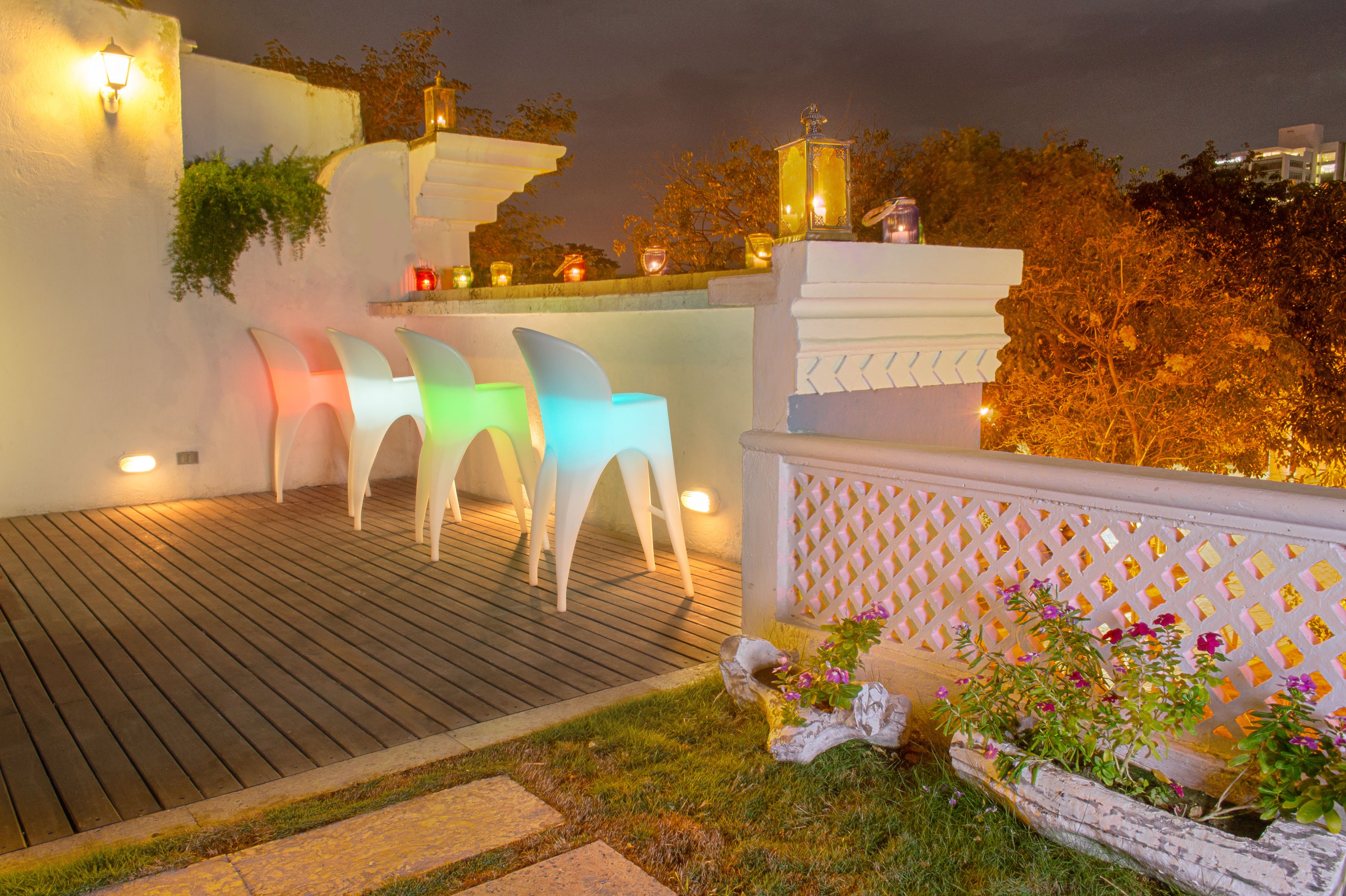 A terrace with white chairs and a wooden deck, surrounded by a white fence and potted plants.