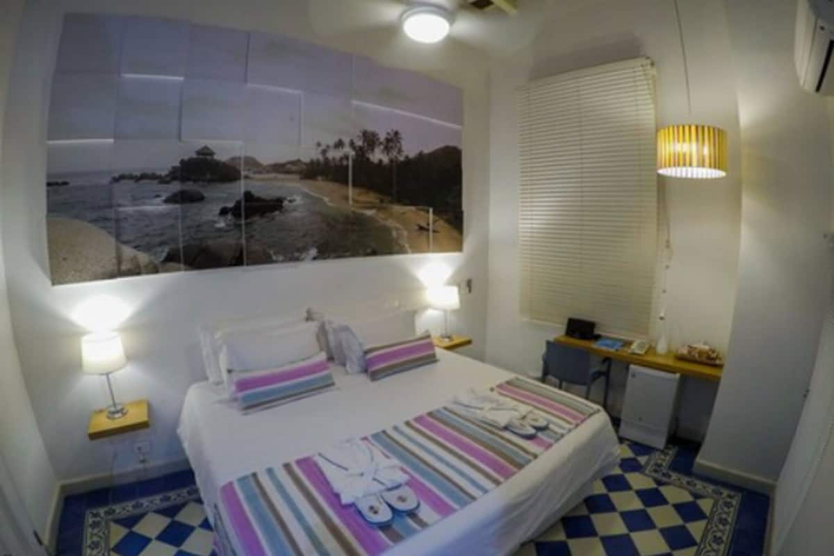 Une chambre à coucher avec un lit, des lampes de chevet, un bureau et une grande fenêtre donnant sur la plage.