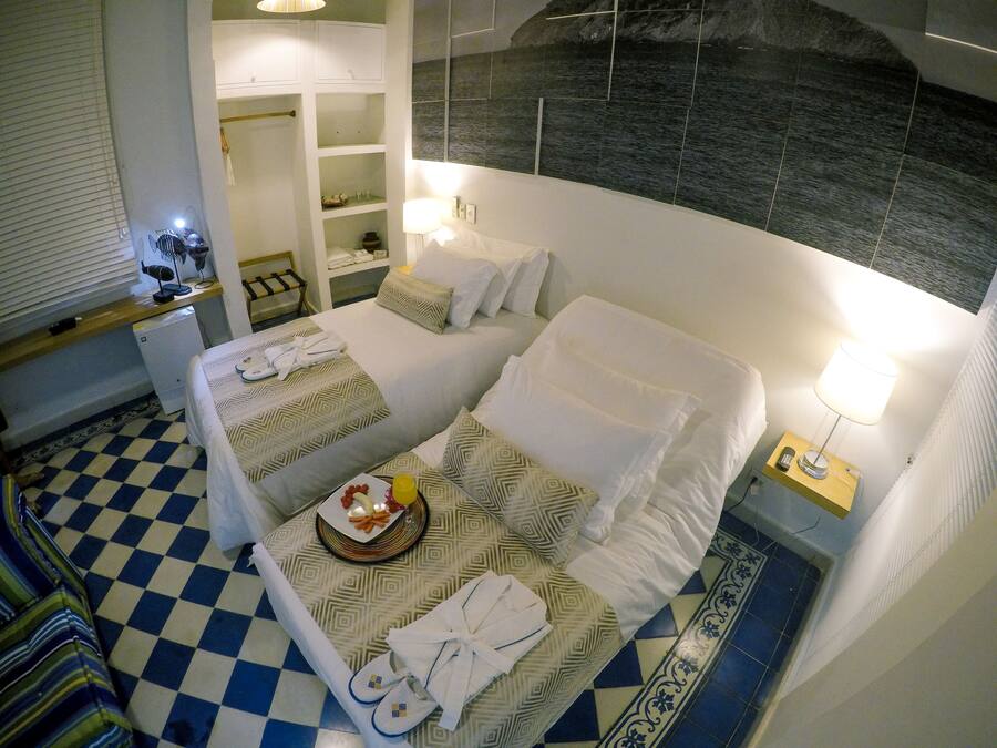 Een hotelkamer met twee bedden, een klein bureau, een stoel, een spiegel en uitzicht op zee.