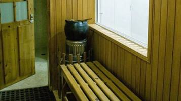 A wooden sauna room with a bench, a large pot, and a window with a lattice design.
