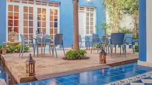 Een patio met blauwe tegels, zitplaatsen, een boom en lantaarns.