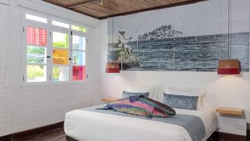 A bedroom with a bed, a colorful fish pillow, a mural of a fisherman, and a window with colorful panes.