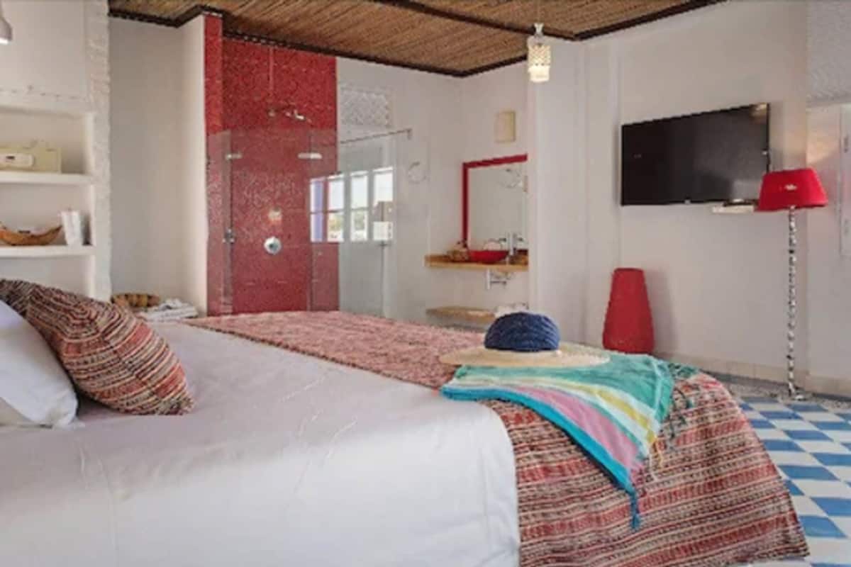 Une chambre d’hôtel avec un lit, une porte rouge, un téléviseur et un sol à carreaux.