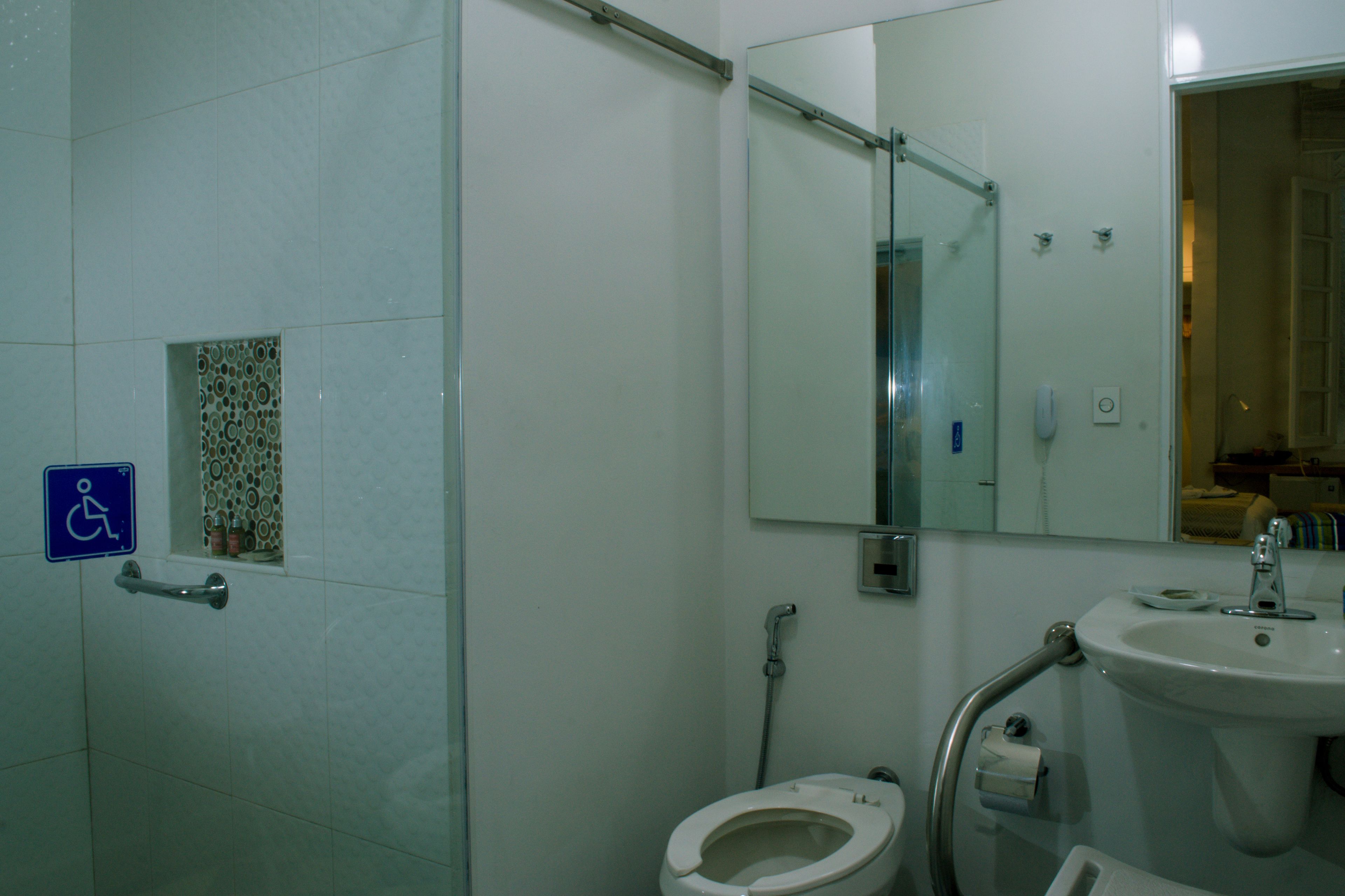 Une salle de bain équipée de toilettes, d’un lavabo et d’un miroir. On y trouve une barre d’appui et un panneau indiquant que les lieux sont accessibles aux personnes en fauteuil roulant.