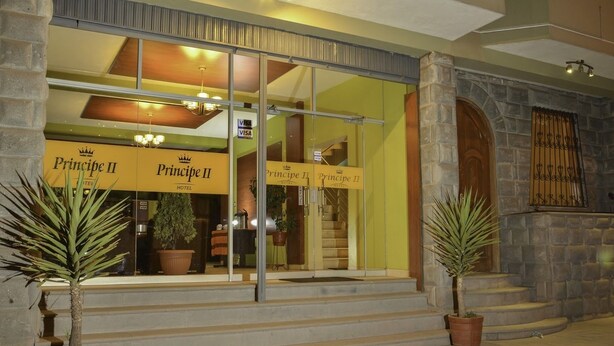 Exterior del Hotel Prince II con entrada de vidrio, fachada de piedra y plantas en macetas al frente.