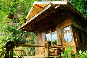 A rustic wooden house with a thatched roof, surrounded by lush greenery. - Pai Treehouse Resort (Pai)
