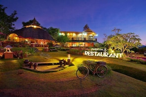 A restaurant with a thatched-roof structure, a covered outdoor seating area, and a well-lit garden path. - Pai Treehouse Resort (Pai)