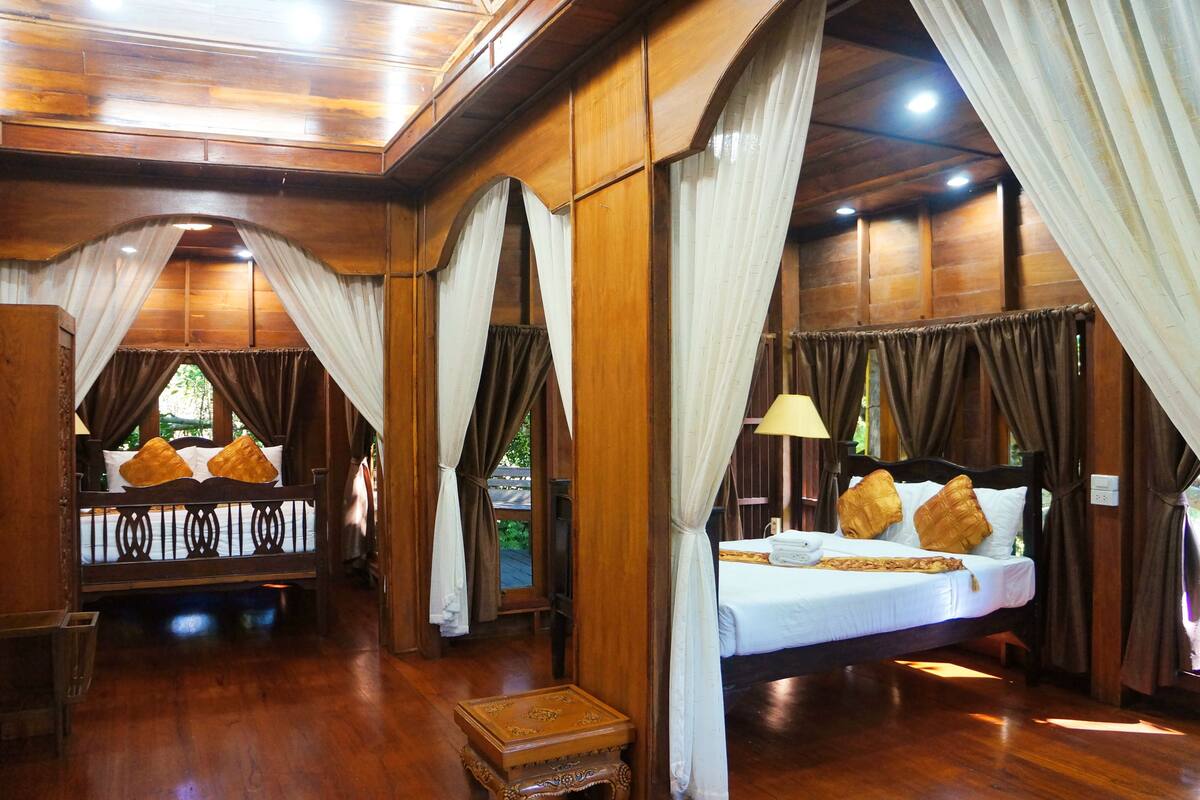 Quarto de madeira com cama, cortinas e uma pequena mesa.