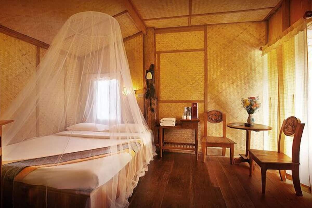 Quarto com cama sob um mosquiteiro, televisão, mesa pequena com um vaso e uma cadeira.