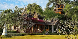 A traditional wooden house with a thatched roof, surrounded by lush greenery and a well-maintained garden. - Pai Treehouse Resort (Pai)