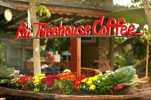 A sign for 'Pai Treehouse Coffee' with a wooden post and colorful flowers in the foreground. - Pai Treehouse Resort (Pai)