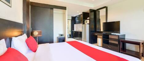 Una camera d'albergo con un letto grande, una TV, angolo cottura e ventilatore a soffitto.