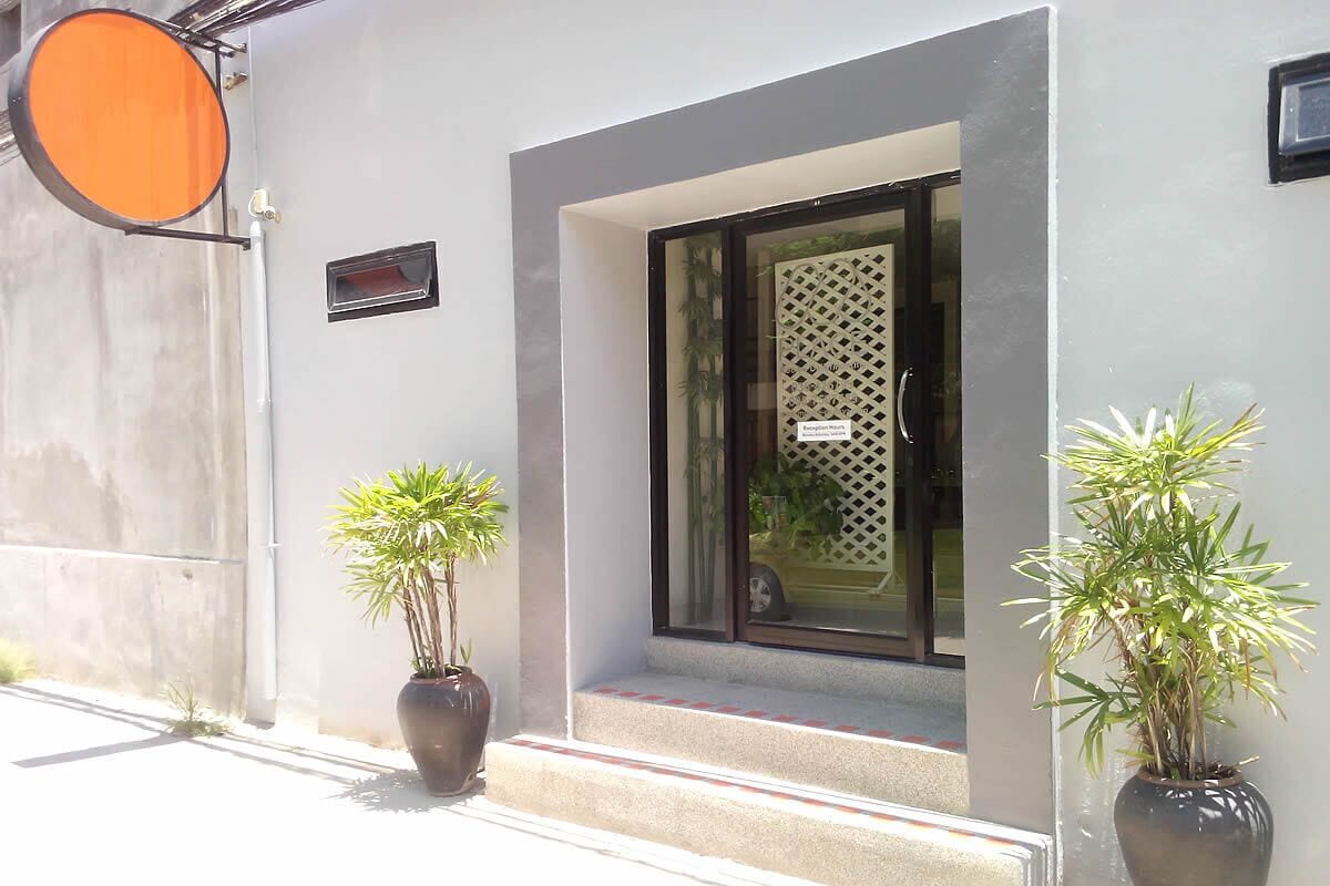 A modern building entrance with a glass door, two potted plants, and a small sign above the door.