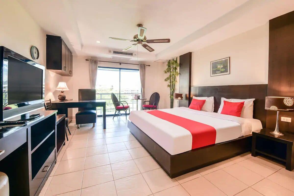 A hotel room with a large bed, a desk with a TV, a chair, a ceiling fan, and a window with curtains.