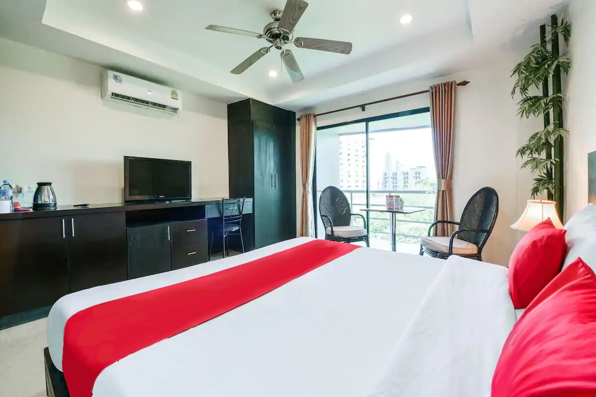 A hotel room with a bed, a desk, a television, and a balcony with chairs.