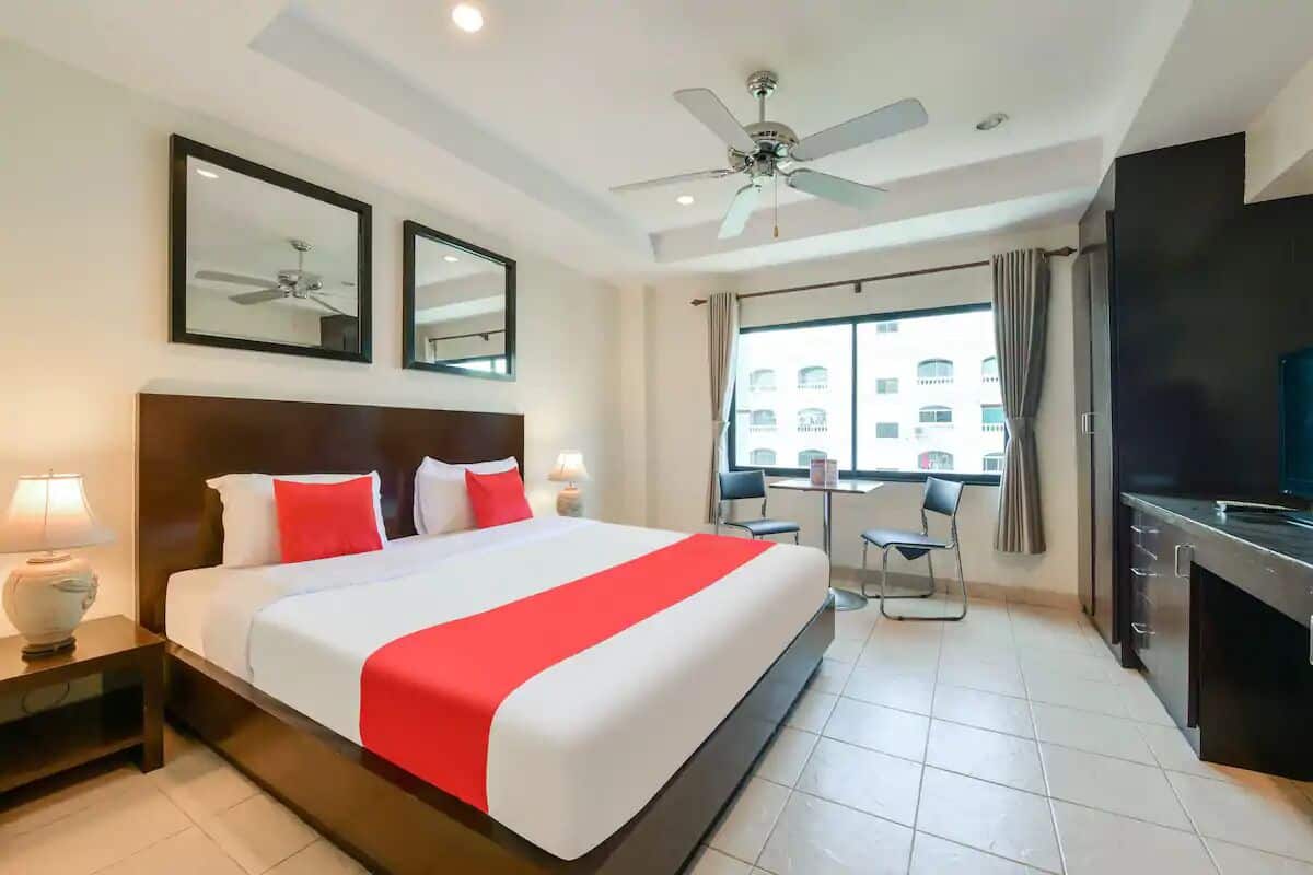 A hotel room with a large bed, a ceiling fan, a TV, a desk, and a window with curtains.