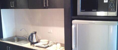 A compact kitchen with dark cabinets, a stainless steel sink, a microwave, and a white refrigerator.