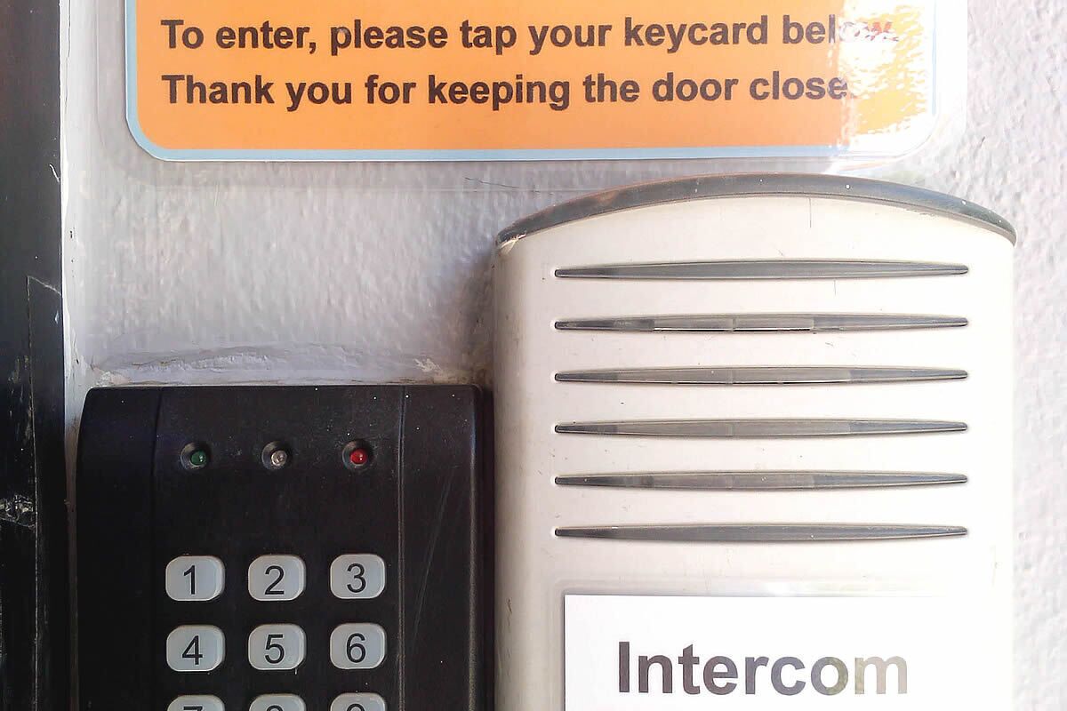 Un teclado numérico y un dispositivo de intercomunicador metálico con un cartel encima.