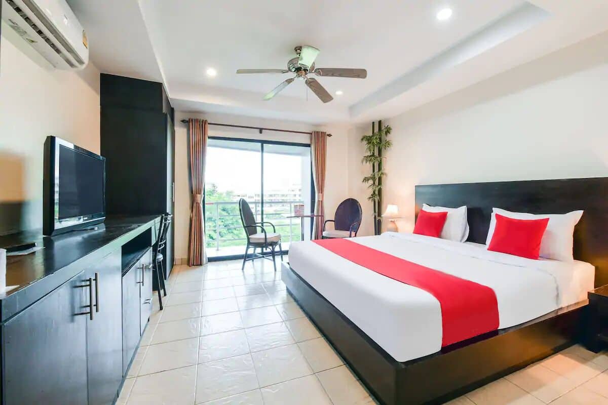A hotel room with a bed, a desk, a television, a ceiling fan, and a view of the outdoors.
