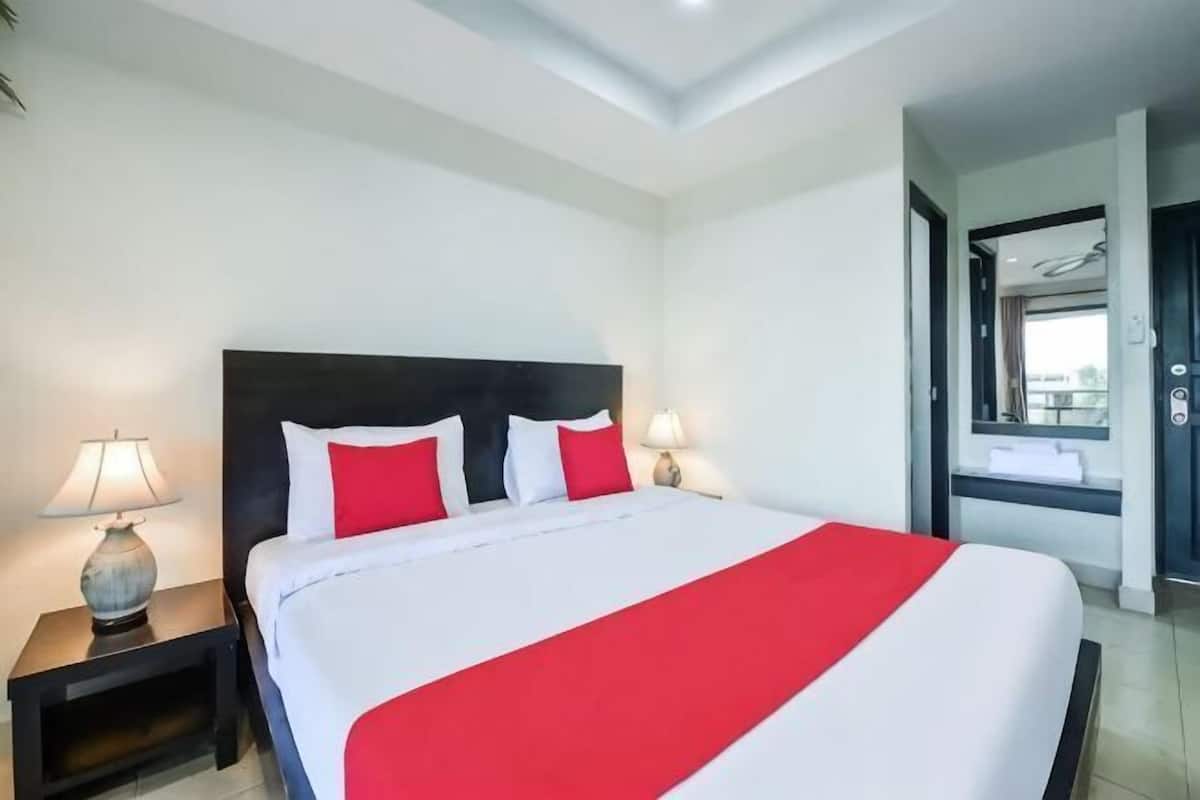 A hotel room with a large bed, two bedside tables with lamps, a window with a view, and a door leading to another room.