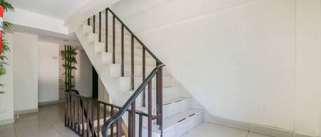 A modern staircase with a metal railing, white walls, and a tiled floor.