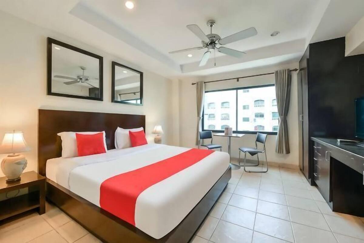 A hotel room with a bed, bedside lamps, a ceiling fan, a window with curtains, and a TV.