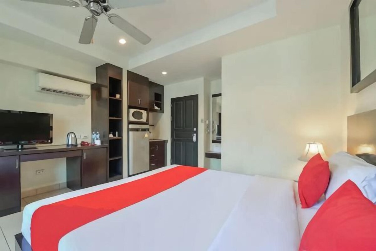 A hotel room with a bed, a desk, a TV, a microwave, and a ceiling fan.