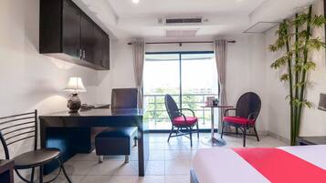 Habitación de hotel con cama, escritorio con lámpara, dos sillas, ventana con cortinas y una planta.