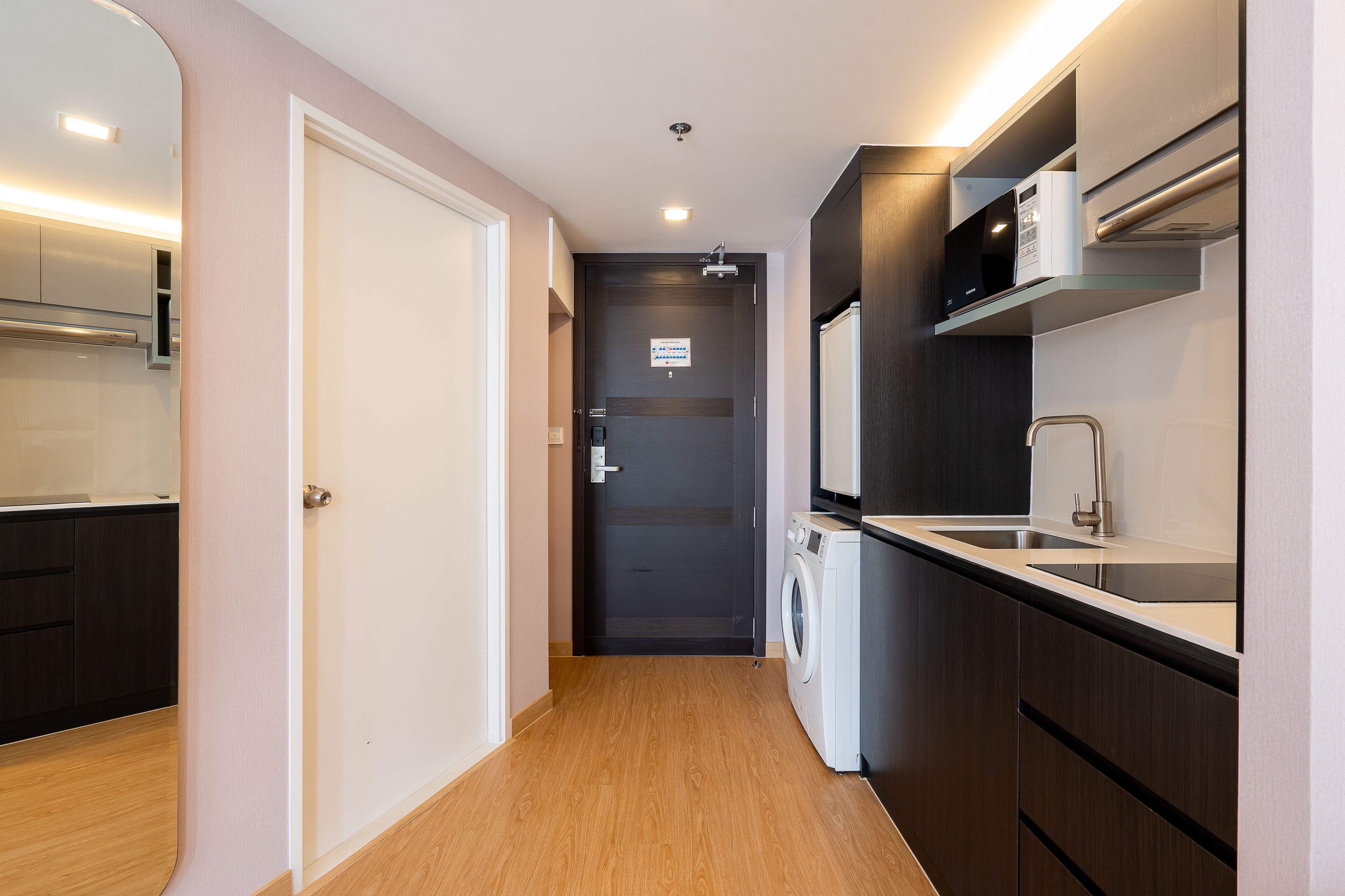 A narrow hallway with a washing machine, a sink, and a door leading to a dark room.