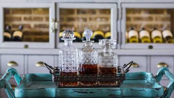 Una botellera con varias botellas y una mesa color turquesa con decantadores de vidrio al frente.