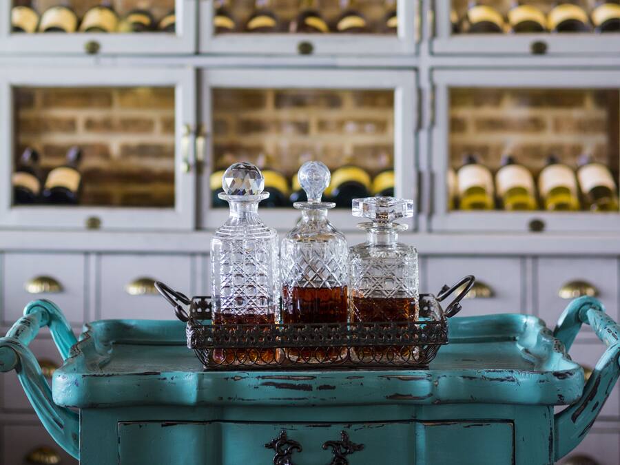 Una botellera con varias botellas y una mesa color turquesa con decantadores de vidrio al frente.