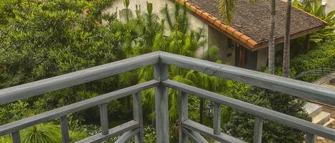 A view from a balcony overlooking a lush garden with a house in the background.