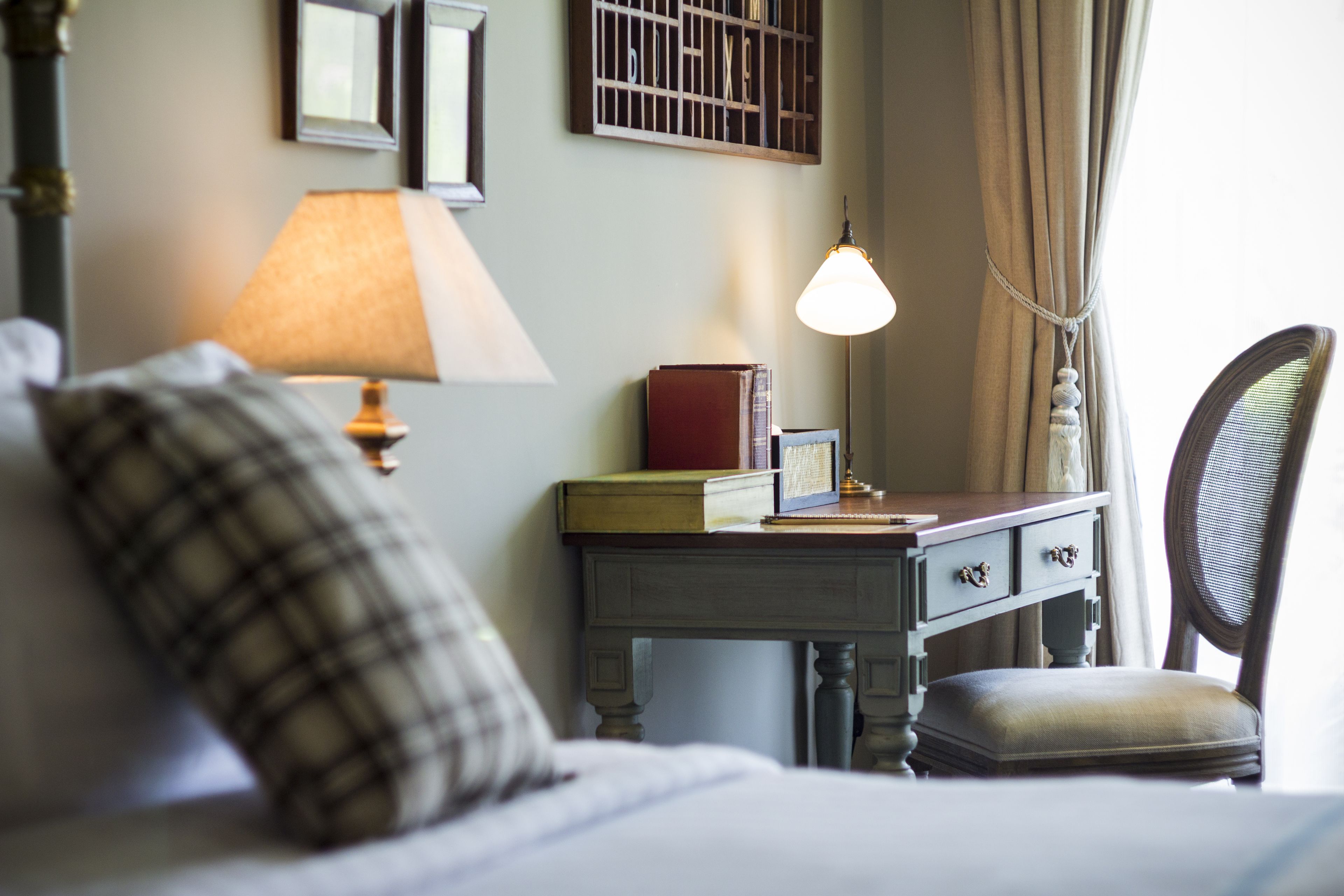 Ein ordentlich eingerichtetes Schlafzimmer mit einem Bett, einem Nachttisch mit Lampe, einem Sessel und einem kleinen Schreibtisch mit Lampe und Büchern.