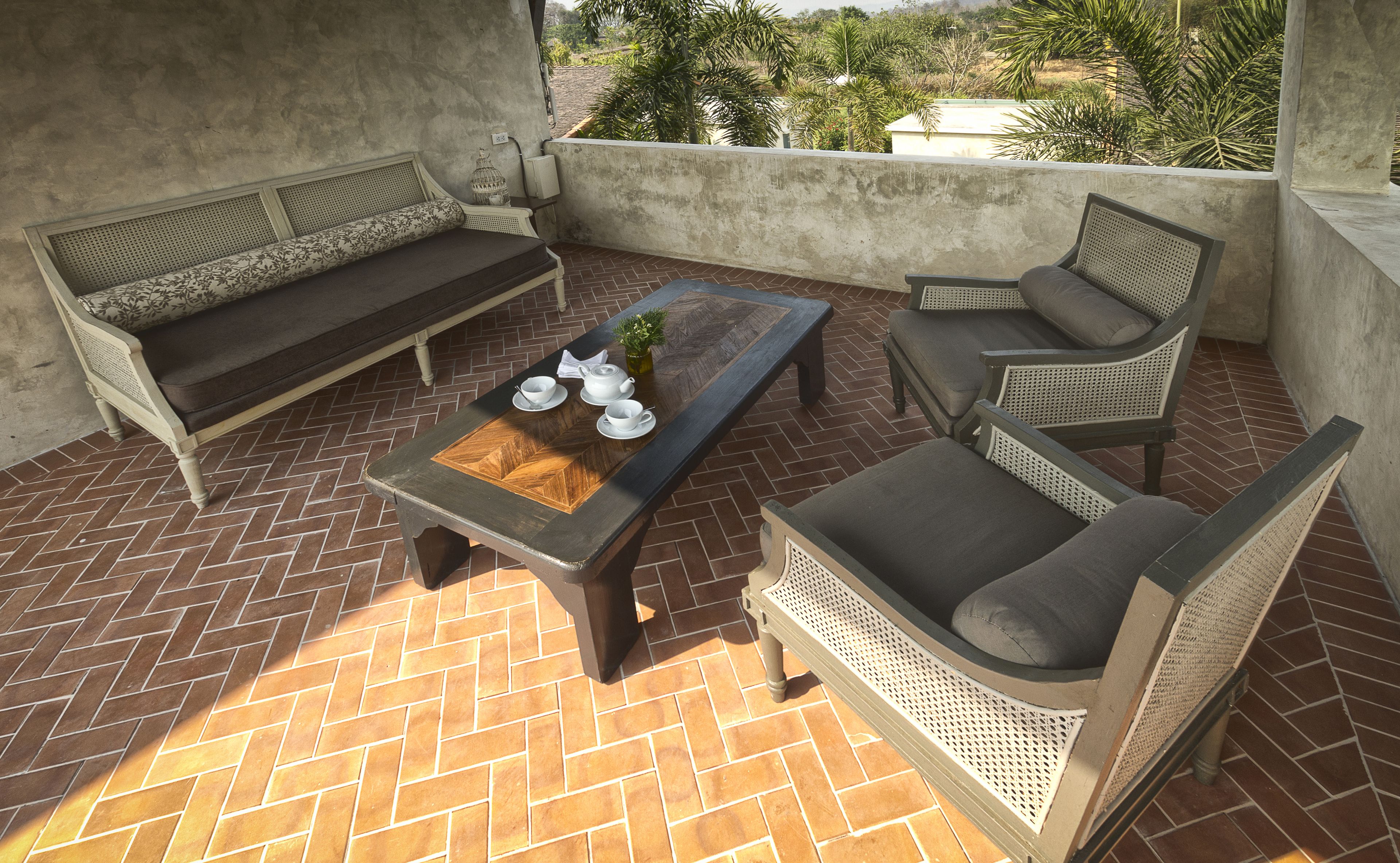A patio with a sofa, armchair, and coffee table, featuring a herringbone tile floor and a view of greenery.