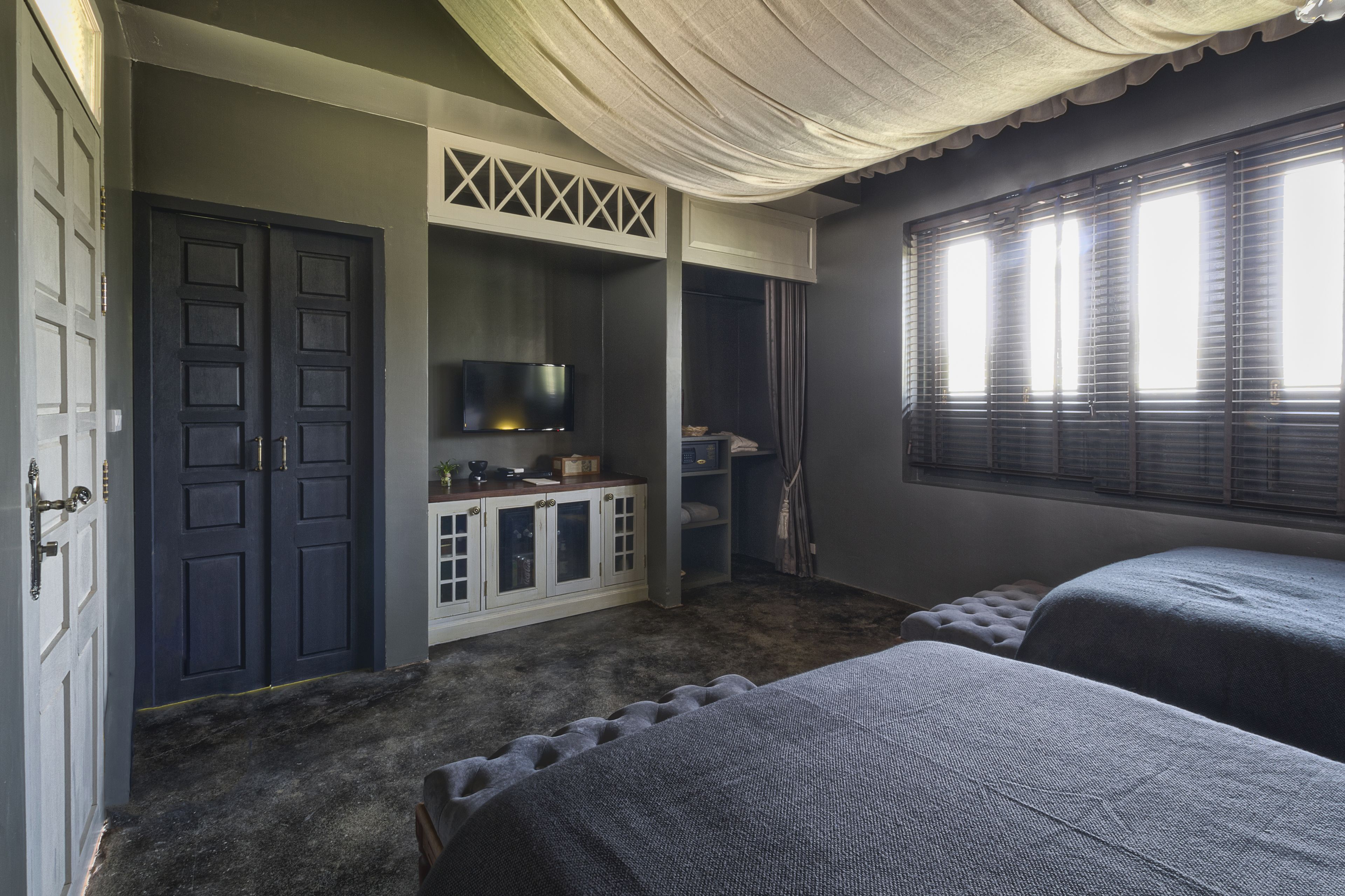 A room with two beds, a TV, a wardrobe, and a window with blinds.