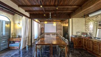 A conference room with a long wooden table, chairs, a projector screen, and a brick wall.