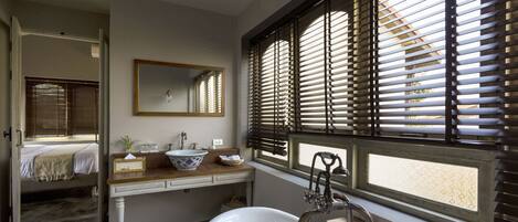 A bathroom with a bathtub, a sink with a mirror, and a window with blinds.