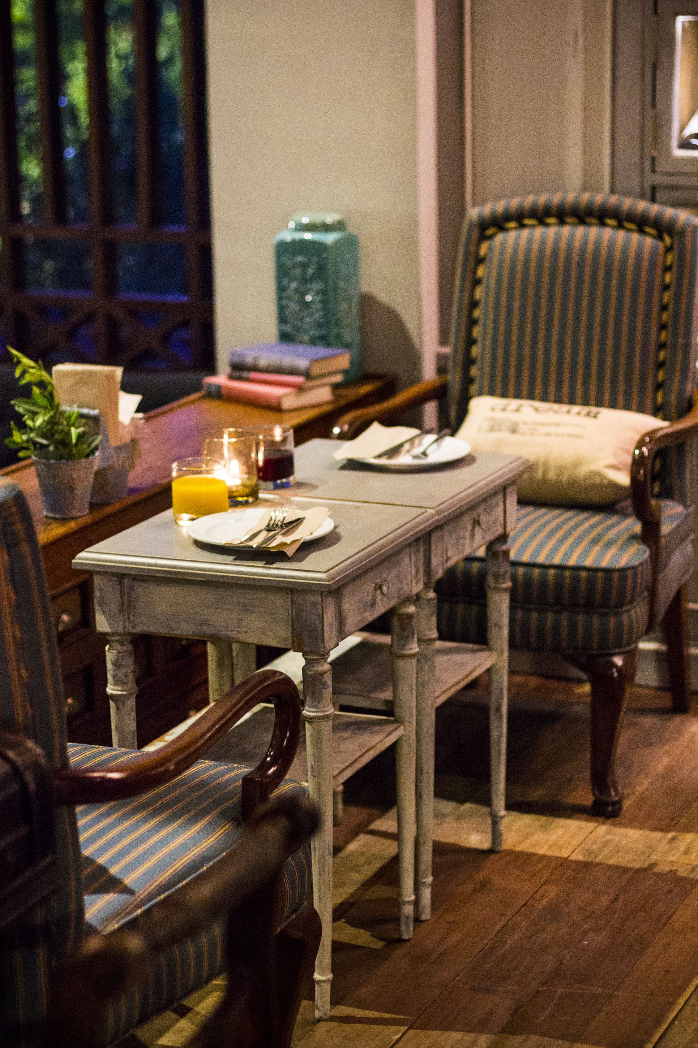 Een eethoek met een houten tafel gedekt voor twee personen, gestreept bekleden stoelen en een kaars op de tafel.