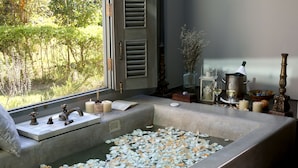 A bathtub filled with water and rose petals, a window with shutters, and various decorative items on a bedside table. - Reverie Siam Resort (Pai)