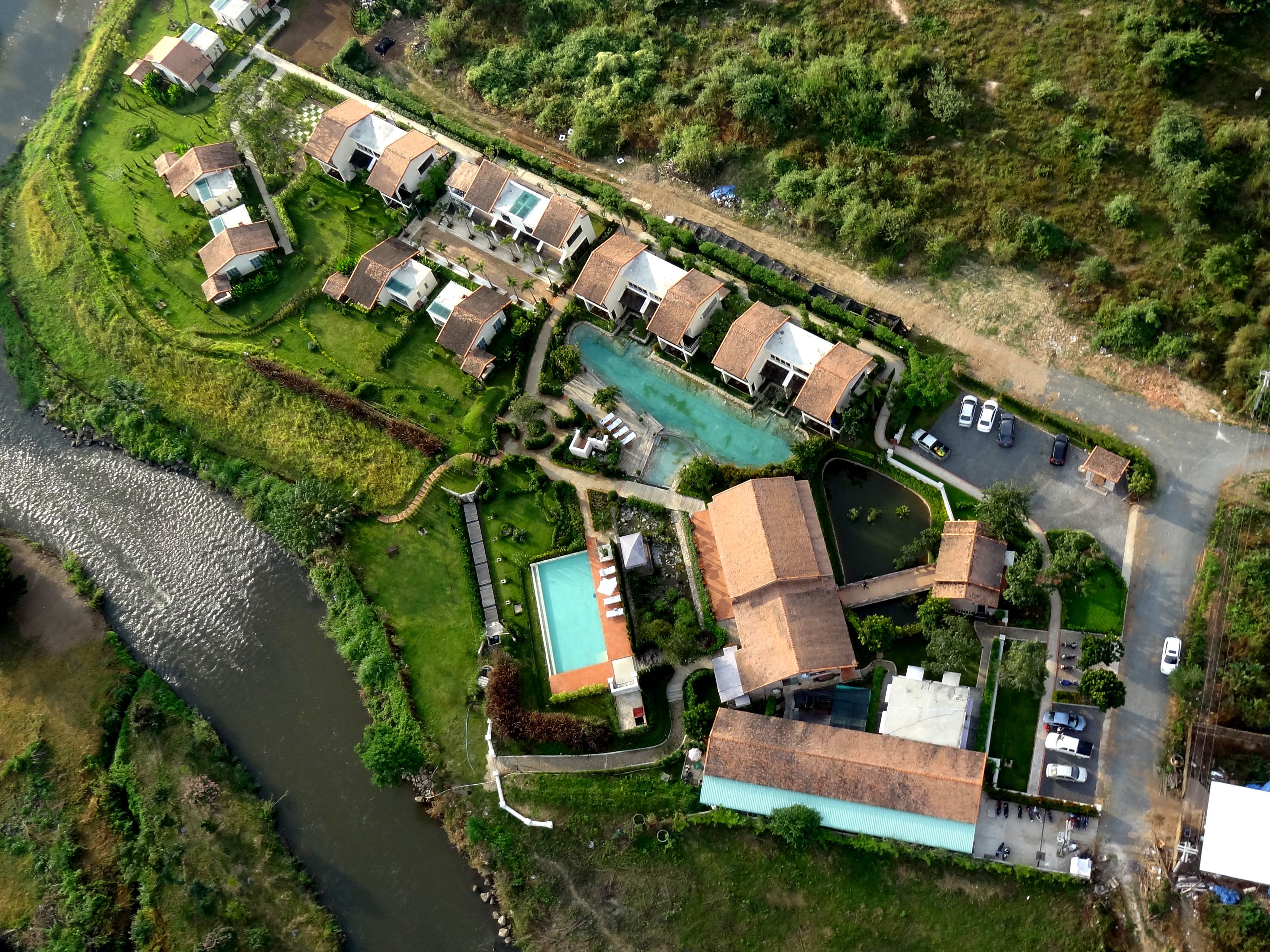 An aerial view of a residential area with houses, a swimming pool, and a river.