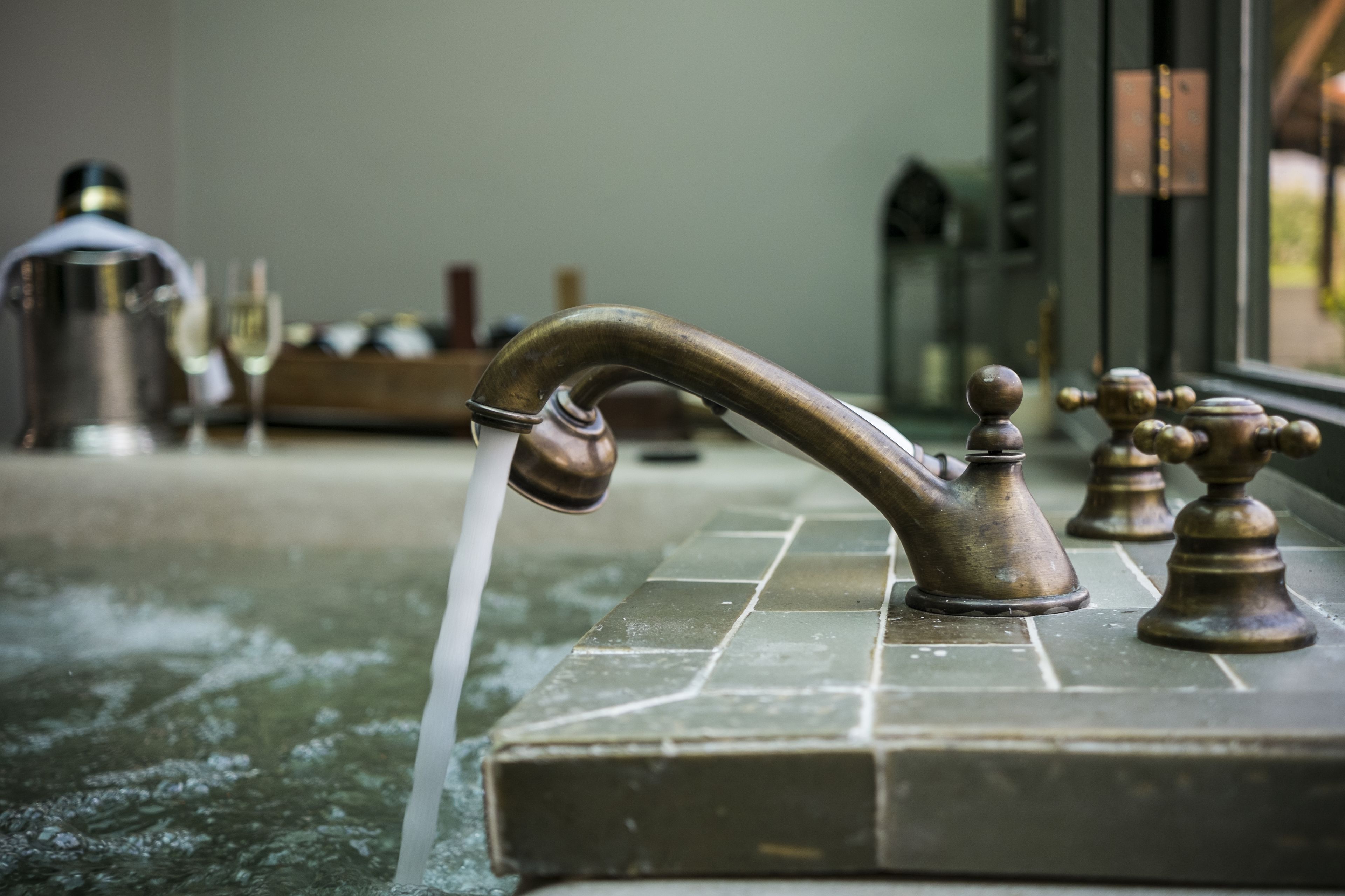 A bathroom with a modern faucet, a bathtub, and a glass of wine on the counter.
