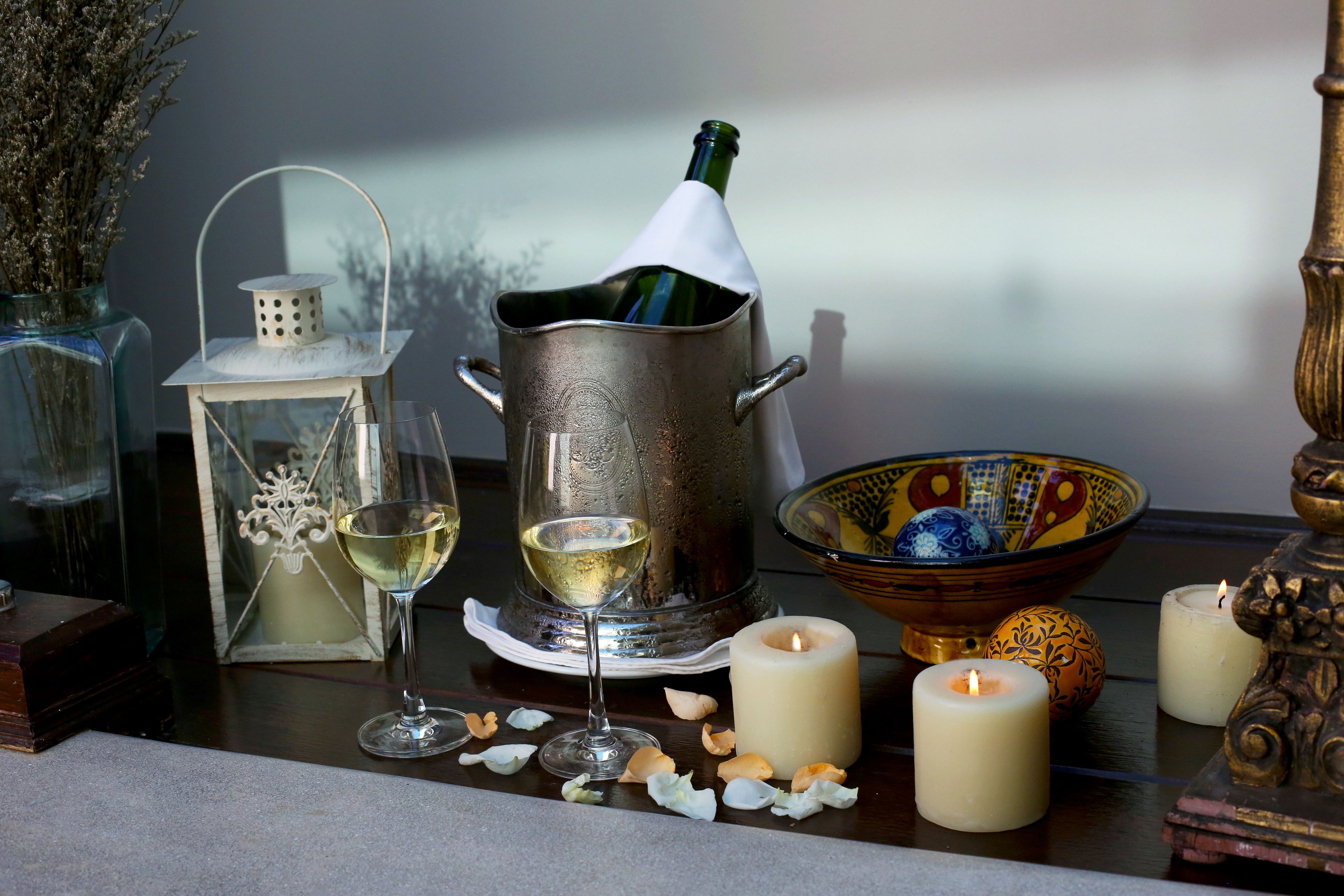 A table with a wine bottle, a glass of wine, candles, decorative items, and a bowl.