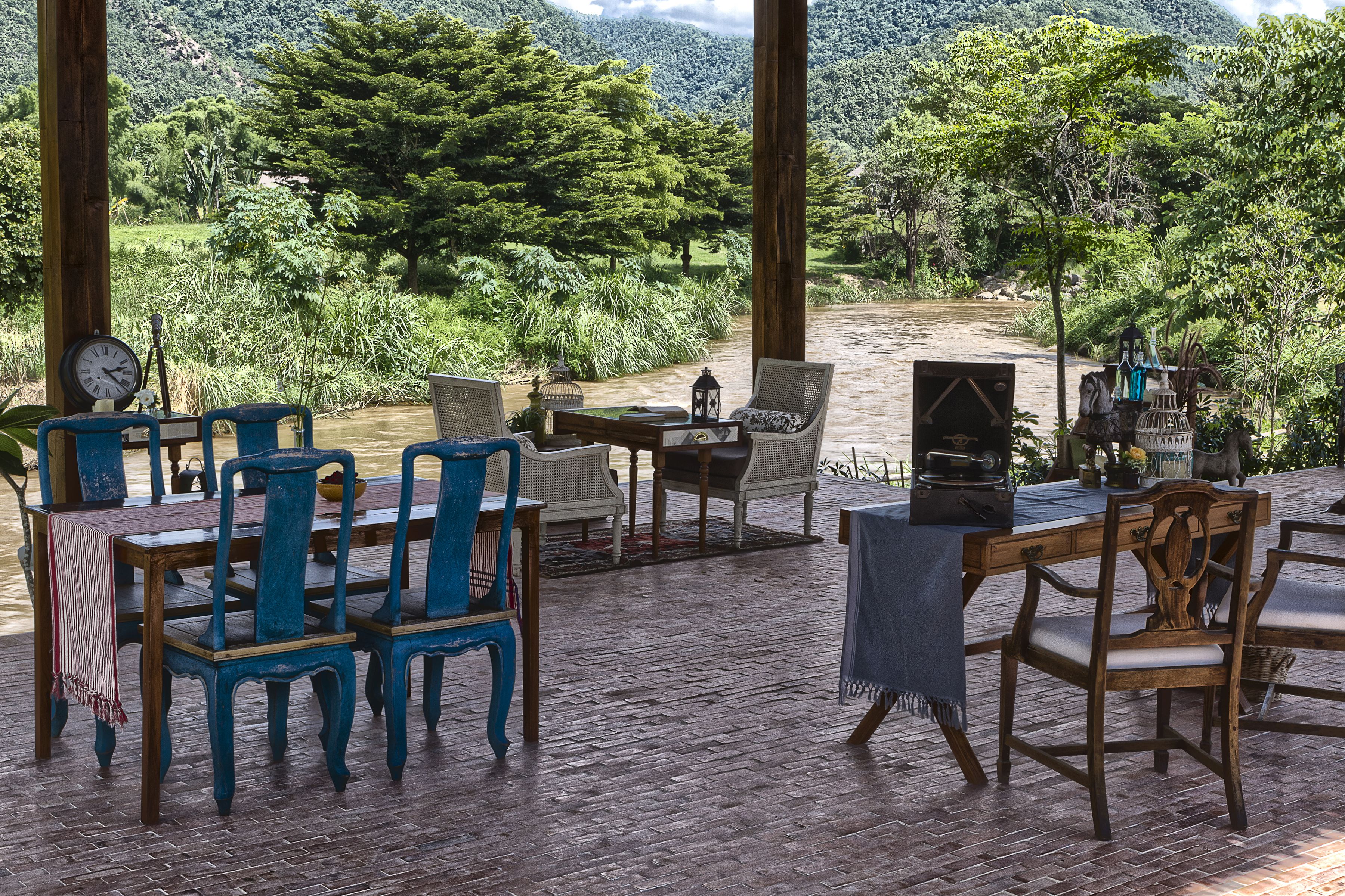 An outdoor patio with wooden furniture, a table, and a view of a river and forested hills.