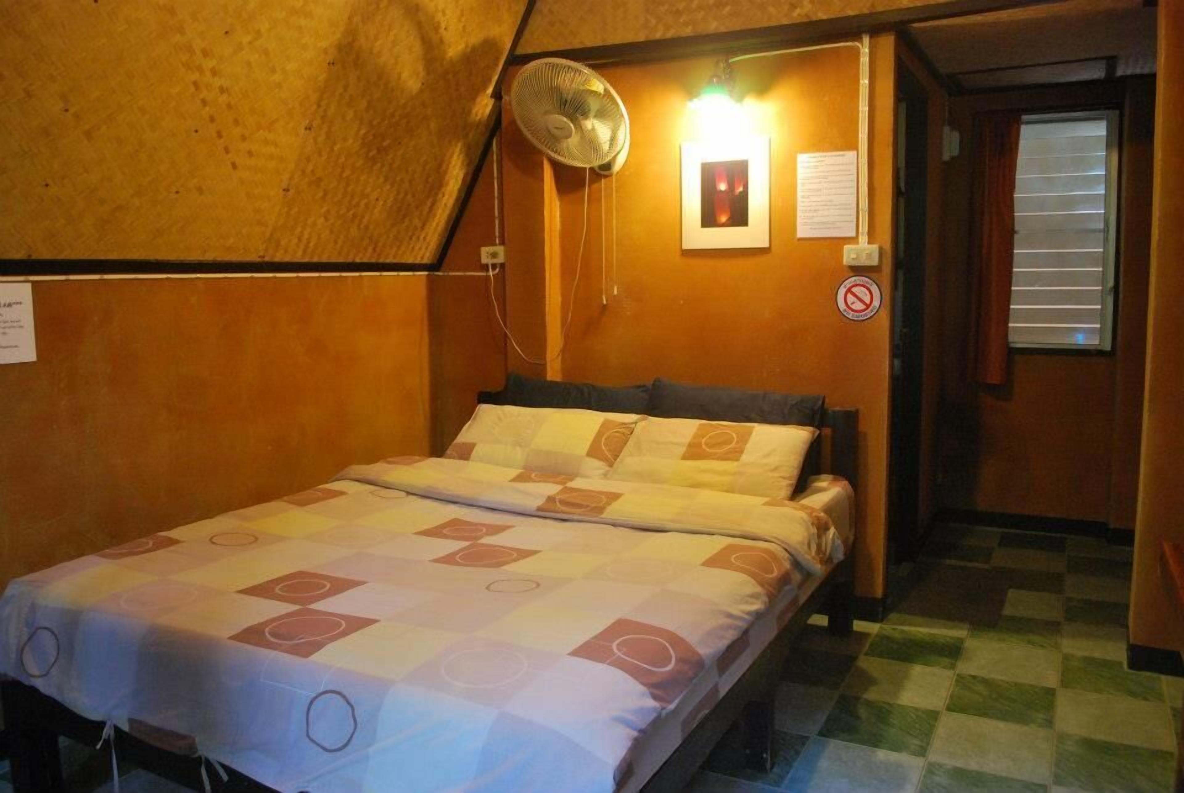 Una habitación pequeña y acogedora con cama, ventilador y ventana con persianas.