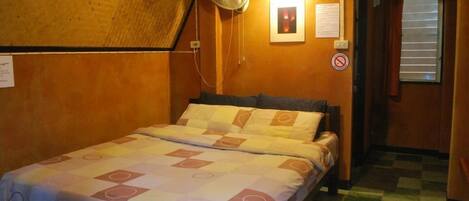 Una habitación pequeña y acogedora con cama, ventilador y ventana con persianas.