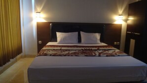 Una habitación de hotel con una cama, dos lámparas de noche, un ventanal con cortinas y suelo de madera.
