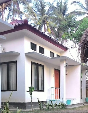 A two-story building with a red roof, white walls, and multiple windows. There is a small porch area with a door and a potted plant.
