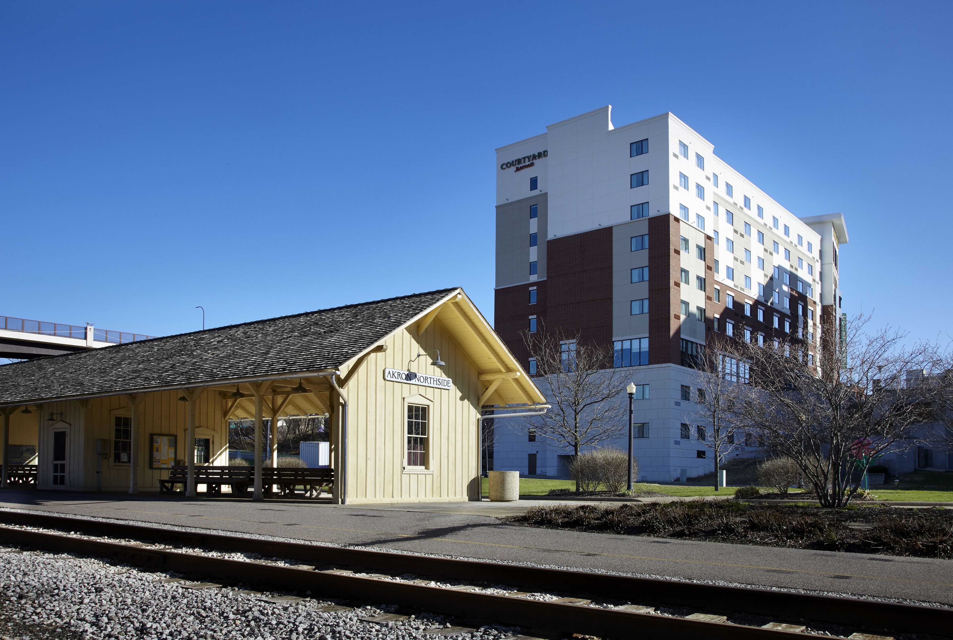 Ein Bahnhof mit einem gelben Gebäude mit der Aufschrift "AKRON NORTHSIDE" und einem modernen Hotel im Hintergrund.