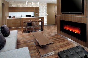 A modern living room with a sofa, a coffee table, a fireplace, and a kitchen area in the background. - Courtyard Akron Downtown (Akron)